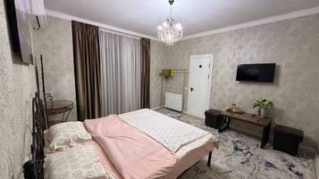 Une chambre à coucher comprenant un lit, un bureau, une chaise, un téléviseur et un lustre.