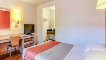 Une chambre d’hôtel avec un lit, un bureau et une chaise, un téléviseur et une salle de bain visible à travers une porte ouverte.
