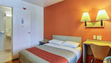 A hotel room with a bed, a desk, a chair, a bathroom, and two wall-mounted lamps.