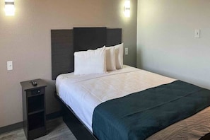 Une chambre d’hôtel avec un lit, une table de chevet et un luminaire fixé au mur.
