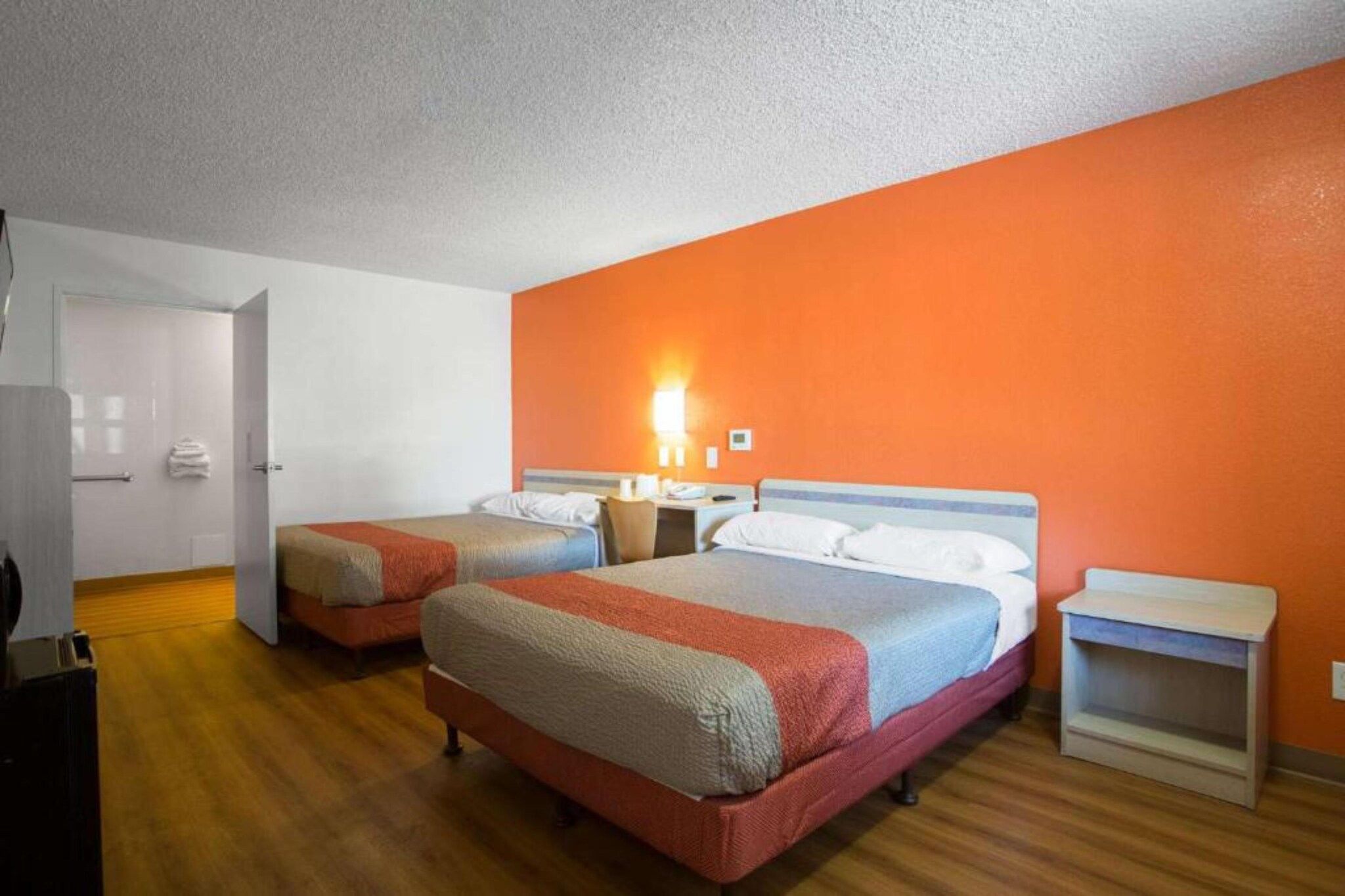 A hotel room with two beds, a wooden floor, a white door, and an orange wall.
