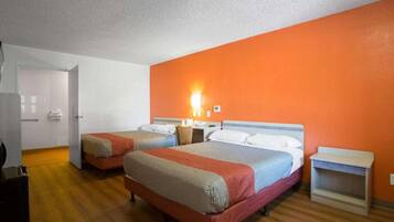 A hotel room with two beds, a wooden floor, a white door, and an orange wall.