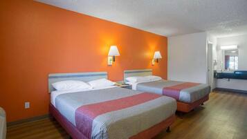 A hotel room with two beds, orange walls, and a bathroom with a mirror and sink.