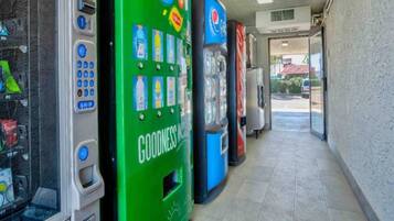 A row of vending machines in a commercial setting with a tiled floor and a view of the outside through a doorway.