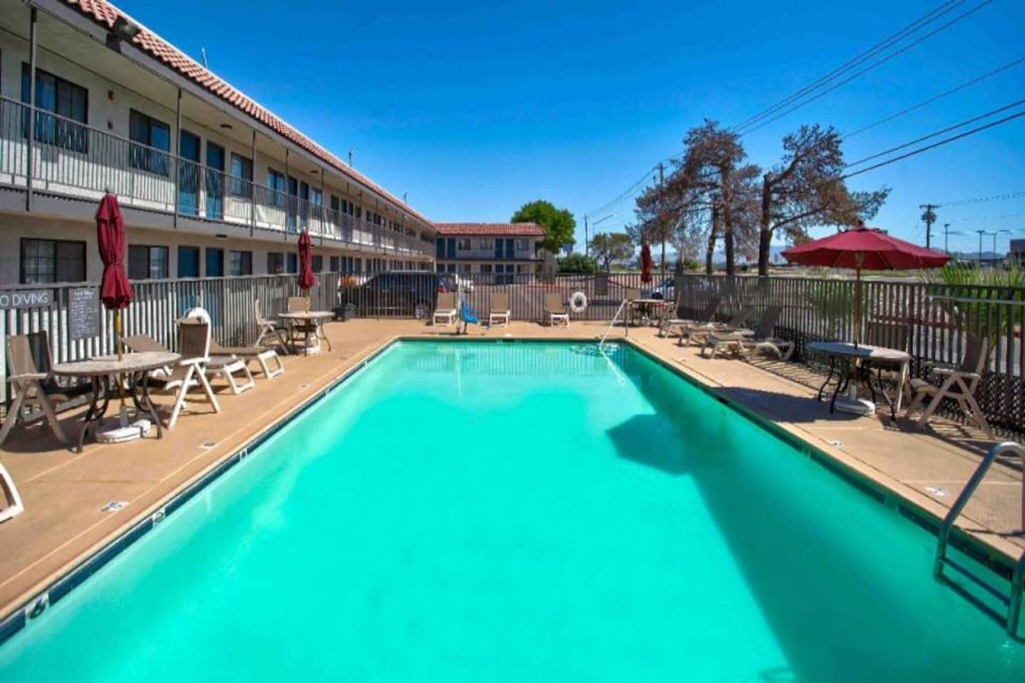 A swimming pool with lounge chairs and umbrellas, surrounded by a building with multiple balconies.