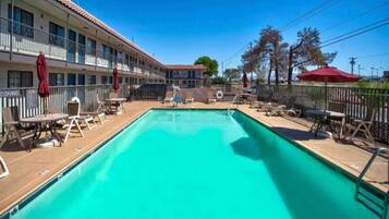 A swimming pool with lounge chairs and umbrellas, surrounded by a building with multiple balconies.