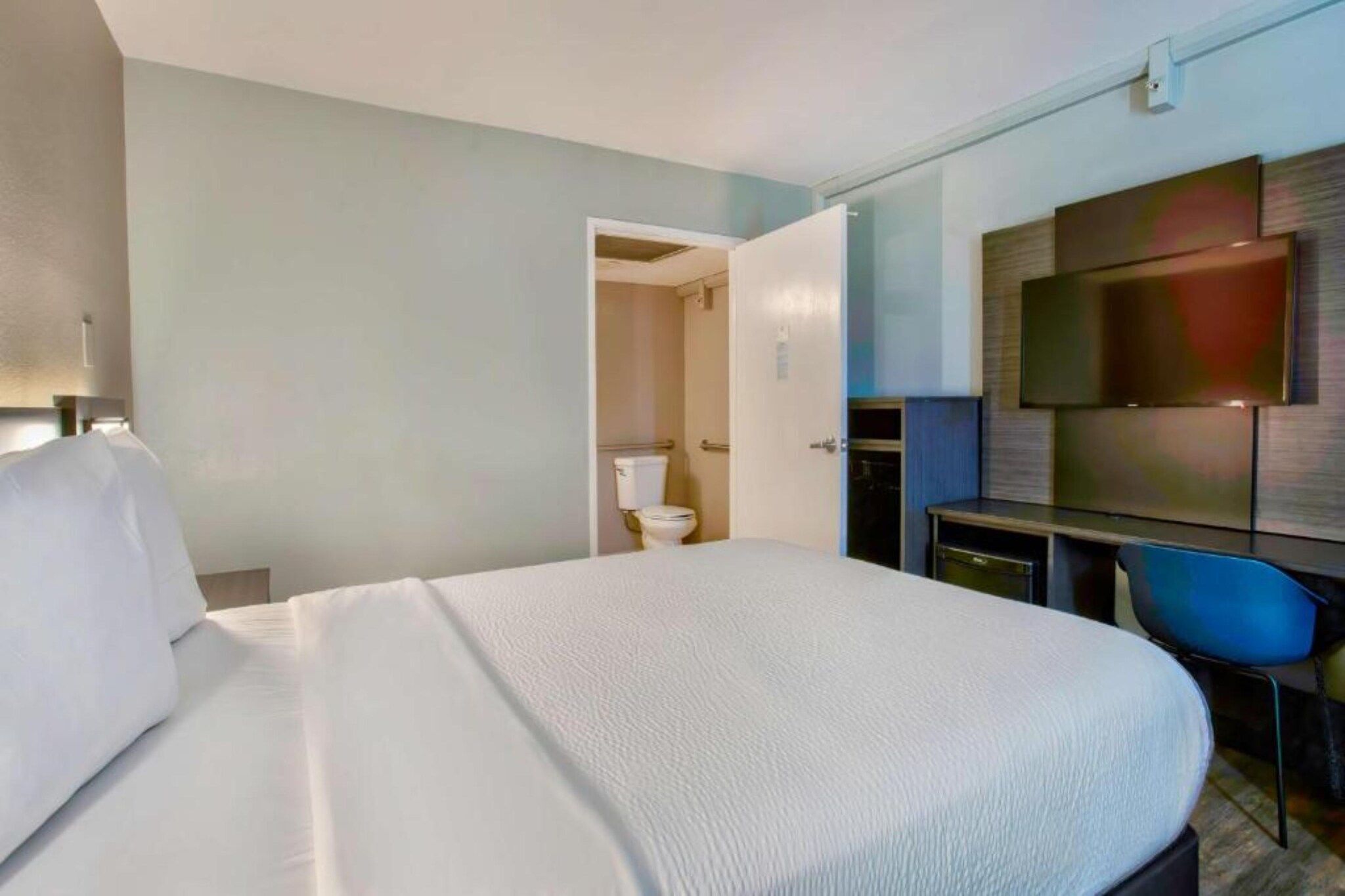 Una camera d'albergo con un letto grande, una scrivania, una sedia, una televisione e un bagno.