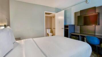 Una camera d'albergo con un letto grande, una scrivania, una sedia, una televisione e un bagno.