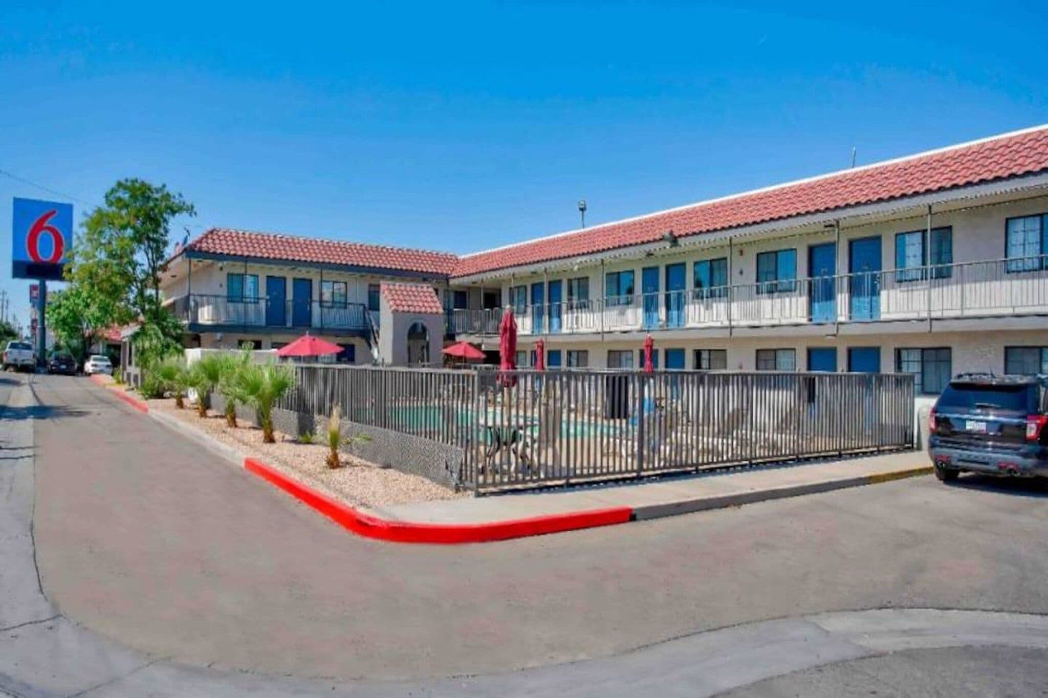 A motel with a red-tiled roof, multiple balconies, and a fenced pool area.
