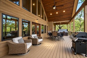 Eine überdachte Terrasse im Freien mit Korbmöbeln, einem Grill und großen Fenstern.