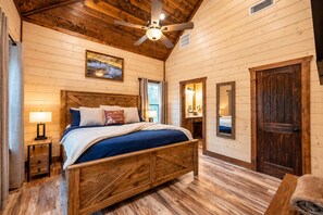 A wooden cabin bedroom with a bed, a ceiling fan, a nightstand, and a window. - Fish Hook Cabin: Hot Tub & Covered Deck (Broken Bow)