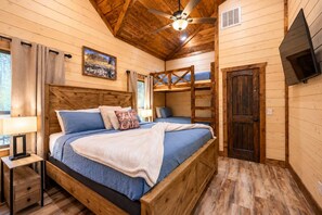 Ein Holzblockhaus-Interieur mit Etagenbett, Einzelbett, Schreibtisch und Wandfernseher.