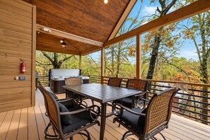 Eine überdachte Terrasse im Freien mit einem Holztisch und Stühlen, einem Whirlpool und Blick auf Bäume.