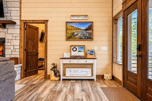 Interior de madera con chimenea, un cuadro de un río, un cartel de bienvenida y una placa.