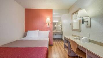 A hotel room with a bed, a desk, a mirror, and a bathroom visible in the background.