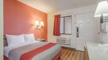 Ein Hotelzimmer mit einem Bett, Nachttischlampen, einem Vorhangfenster, einer Tür und einem Tisch mit Tassen.