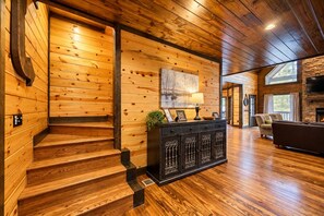 A wooden staircase leading to a living area with a fireplace and a seating area. - Broken Bow Lodge: Hot Tub, Sleeps 18 (Broken Bow)