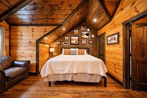 Een slaapkamer in een blokhut met een bed, een leren fauteuil, houten wanden en ingelijste foto's.