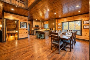 Een houten chalet van binnen met een eethoek, keuken en een trap naar een slaapverdieping.