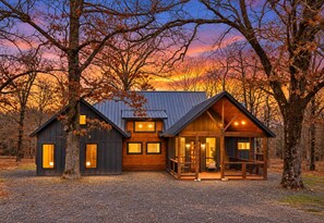 A cabin with a sloped roof, large windows, and a porch with railings. - Modern Cabin w/ Deck & Hot Tub (Broken Bow)