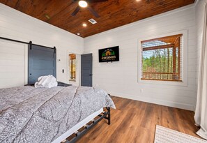 A bedroom with a bed, a window with blinds, a door, and a sign on the wall. - Modern Cabin w/ Deck & Hot Tub (Broken Bow)