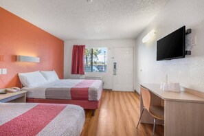 Hotellihuone, jossa on kaksi sänkyä, työpöytä, tuoli, televisio ja ikkuna, jossa on verhot.