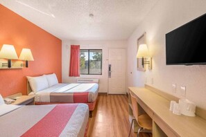 Hotellihuone, jossa on kaksi sänkyä, työpöytä, tuoli, televisio ja ikkuna, jossa on verhot.