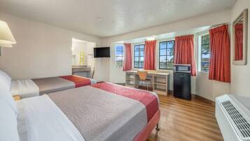 A hotel room with two beds, a desk, a television, and a kitchenette.