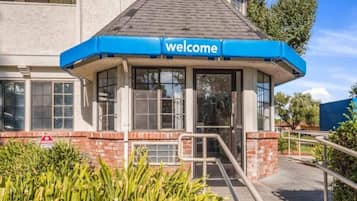 A building entrance with a blue 'welcome' sign, a brick facade, and a glass door.