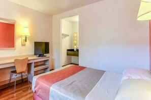 Habitación de hotel con cama, escritorio con silla, televisor y baño visible a través de una puerta abierta.