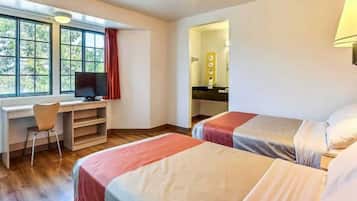 A room with two beds, a desk with a chair, a television, and a window with curtains.