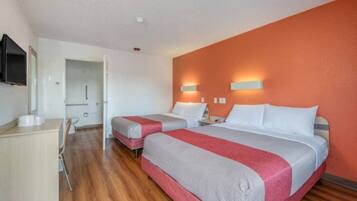 A hotel room with two beds, a desk, and a television.