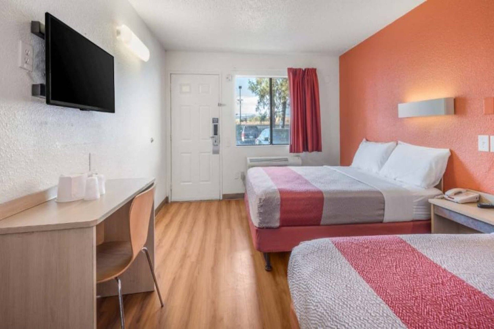 Una habitación de hotel con cama, escritorio, silla, televisor y ventana con cortinas.