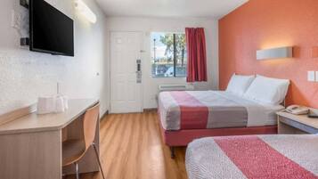 Una habitación de hotel con cama, escritorio, silla, televisor y ventana con cortinas.