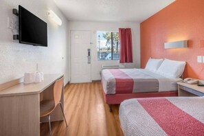 Una habitación de hotel con cama, escritorio, silla, televisor y ventana con cortinas.