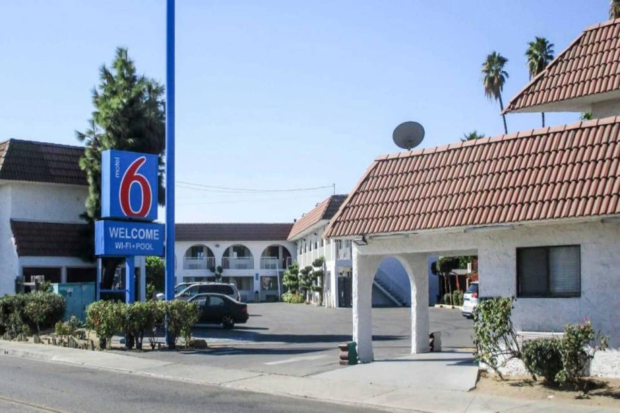 Um motel com uma placa visível indicando o número 6. Há uma placa de boas-vindas acima da entrada, e o edifício apresenta um estilo arquitetônico tradicional com telhado de telhas.