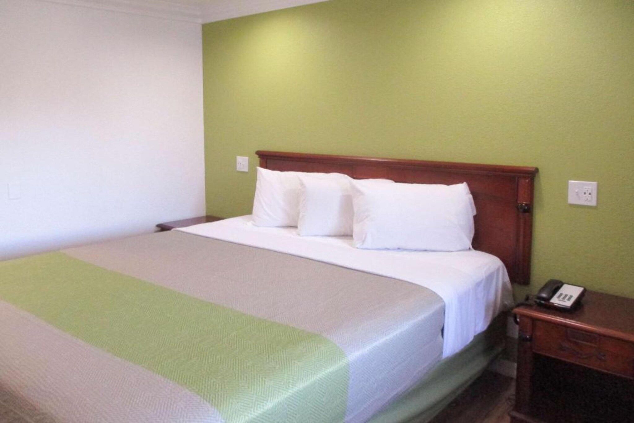 A single bed with a wooden headboard, white bedding, and a bedside table with a telephone.