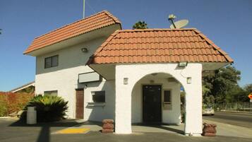 A two-story building with a red-tiled roof, a satellite dish, and a small entrance with an archway.