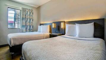 A hotel room with two beds, a window with patterned curtains, and a nightstand with a lamp.