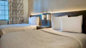 A hotel room with two beds, a window with patterned curtains, and a wall-mounted light fixture.