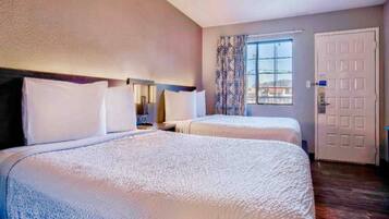 A hotel room with two beds, a window with curtains, a door, and a nightstand.