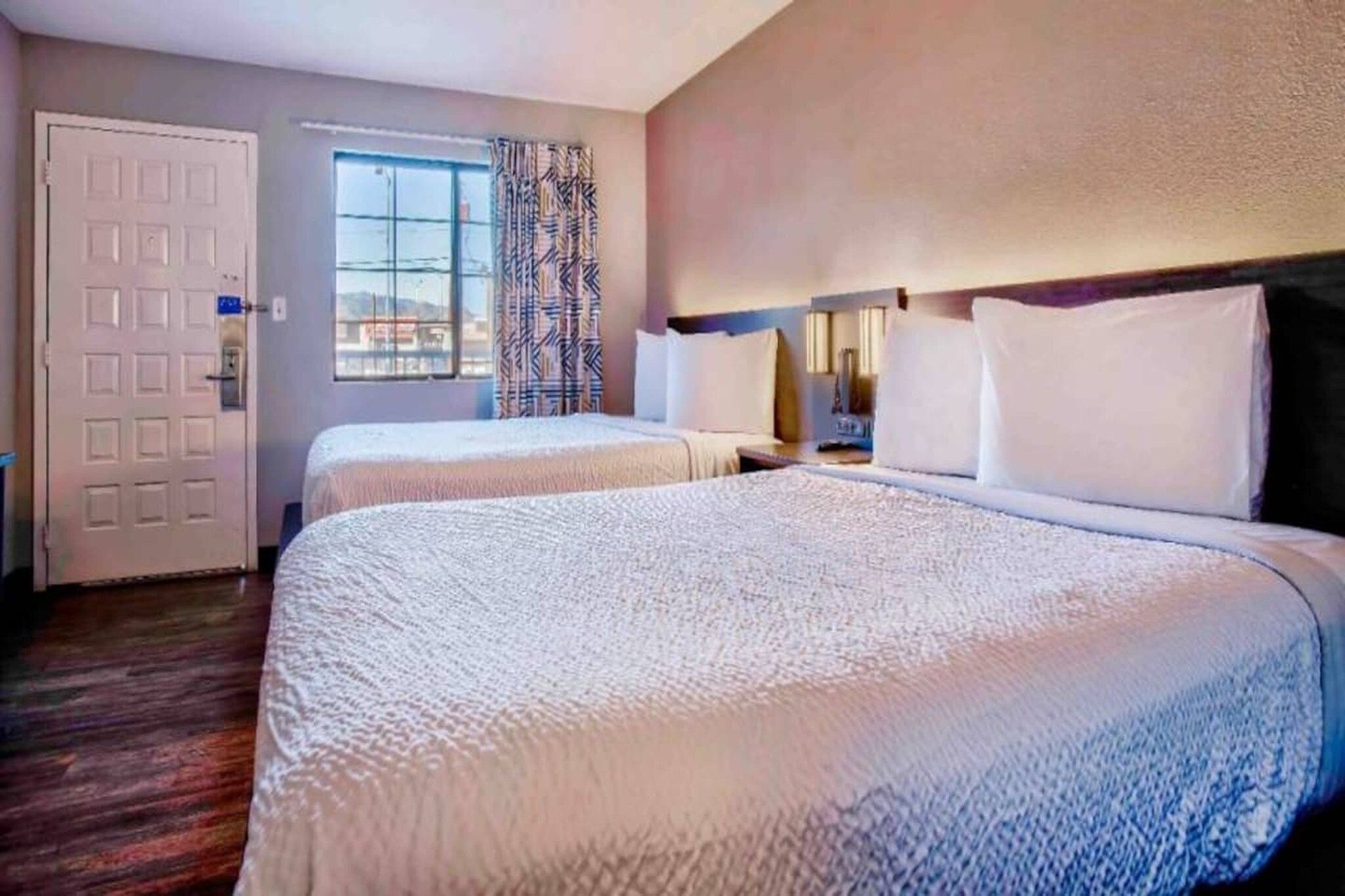 Een hotelkamer met twee bedden, een raam met gordijnen, een deur en uitzicht op de omgeving.