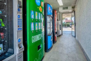 A row of vending machines in a commercial setting with a tiled floor and a view of the outside through a doorway. - 2 Queen Beds | Mini Fridge (Kingman)