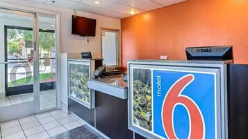 A reception desk with a large sign indicating room number 6, a flat-screen TV mounted on the wall, and a Dell computer on top of the desk.