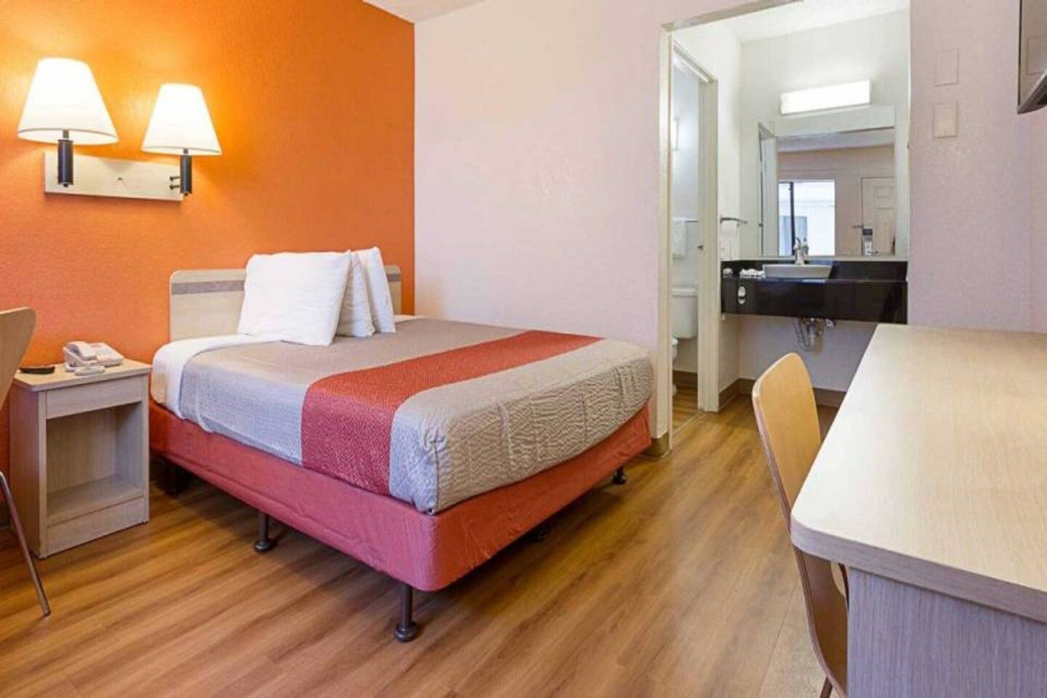A hotel room with a bed, bedside table, lamp, and a view into the bathroom.