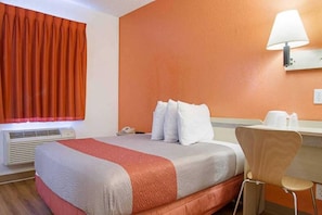 Ein Hotelzimmer mit Bett, Schreibtisch, Stuhl, Lampe und einem fensterbepflanzten Fenster.