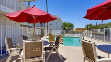 A poolside area with lounge chairs and umbrellas, a pool, and a fenced area.