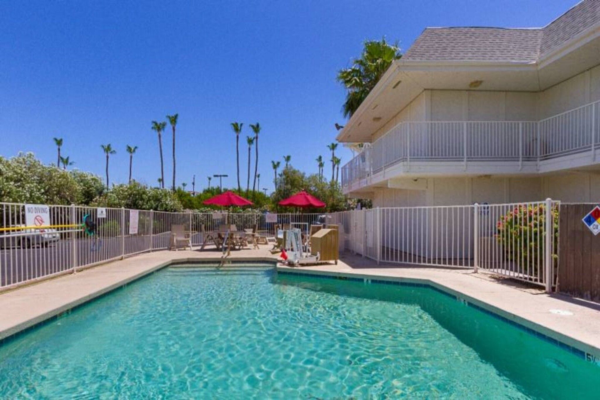 A swimming pool with a fenced area, palm trees, and a building with balconies.