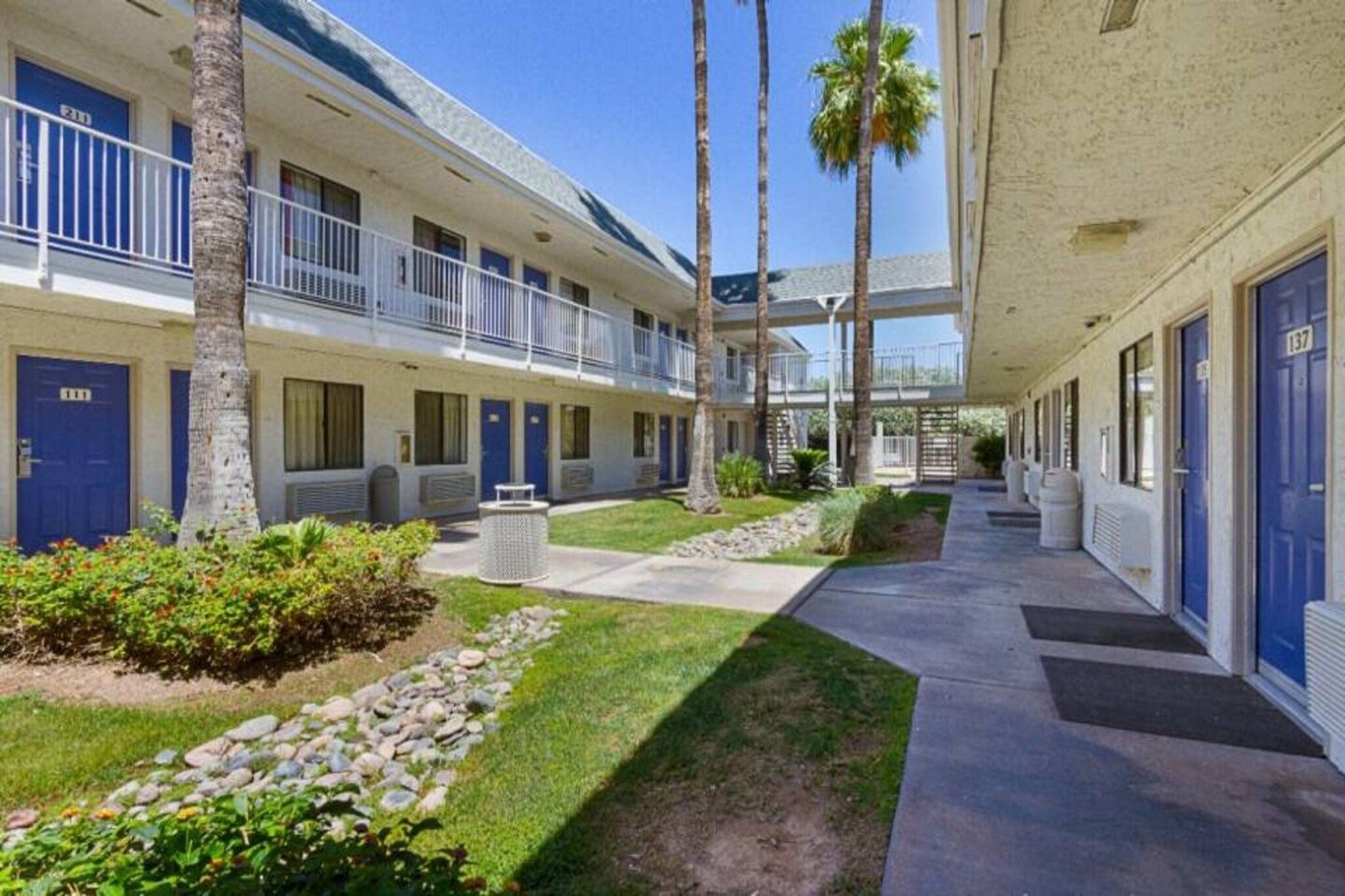 A hotel with a covered walkway, palm trees, and a well-maintained lawn.