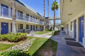 A hotel with a covered walkway, palm trees, and a well-maintained lawn. - 1 Queen bed | Mesa, AZ - South (MESA)